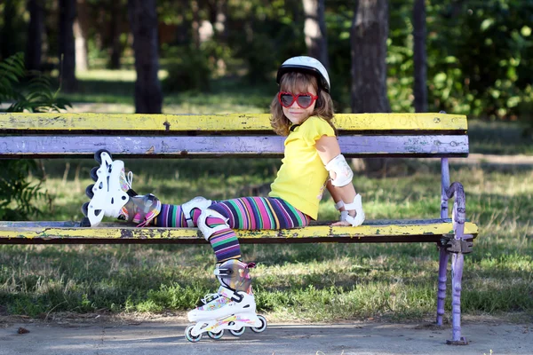 Bambina con pattini a rotelle seduta sulla panchina — Foto Stock