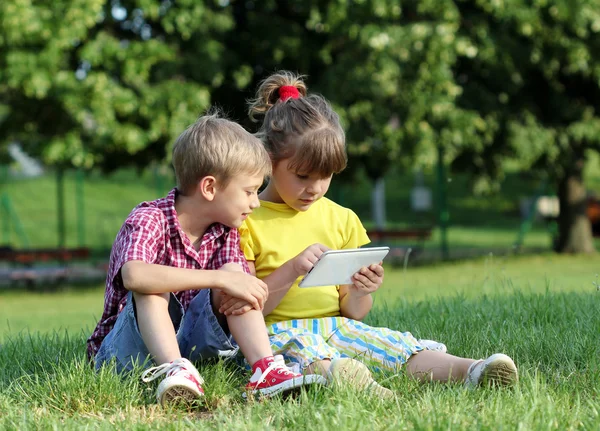 Liten flicka och en pojke med tablett i park — Stockfoto