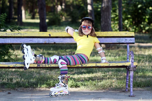 Маленька дівчинка з роликовими ковзанами і шоломом сидить на лавці — стокове фото