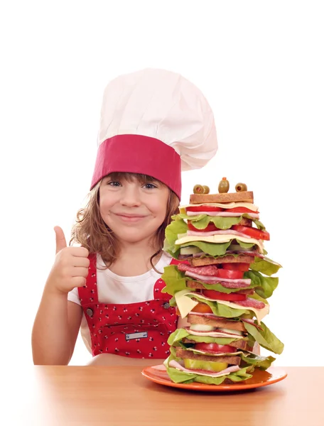 Little girl cook with tall sandwich and thumb up — Stock Photo, Image