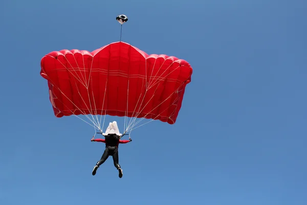 Parachutist met rode parachute op blauwe hemel — Stockfoto