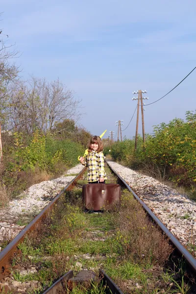 Little girl with suitcase and umbrella standing on railroad — Stock Photo, Image
