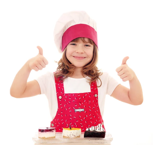 Heureux petite fille cuisinier avec pouces vers le haut et gâteaux — Photo