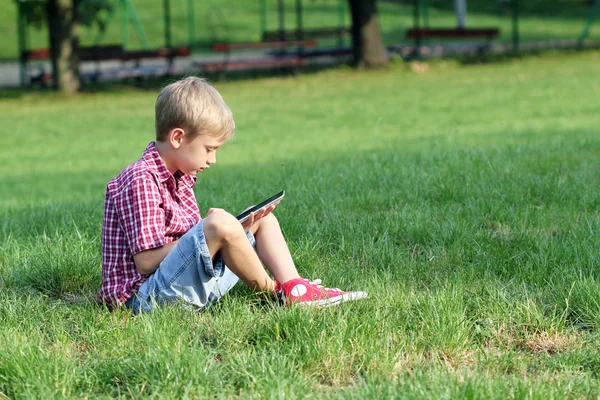 Menino sentado na grama e jogar com tablet pc — Fotografia de Stock