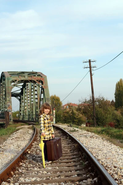 Little girl with umbrella and suitcase on railroad — Stock Photo, Image