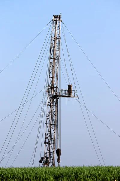 Oil drilling rig behind green wheat field — Stock Photo, Image