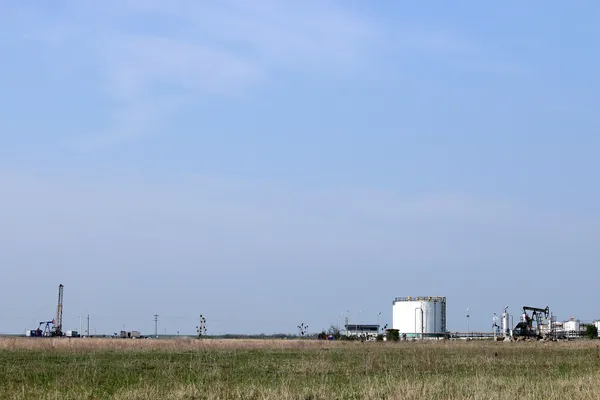 Campo petrolífero con plataforma de perforación terrestre bomba de aceite jack y tanques de refinería —  Fotos de Stock