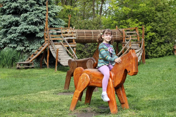 Menina feliz no parque infantil com cavalos de madeira — Fotografia de Stock