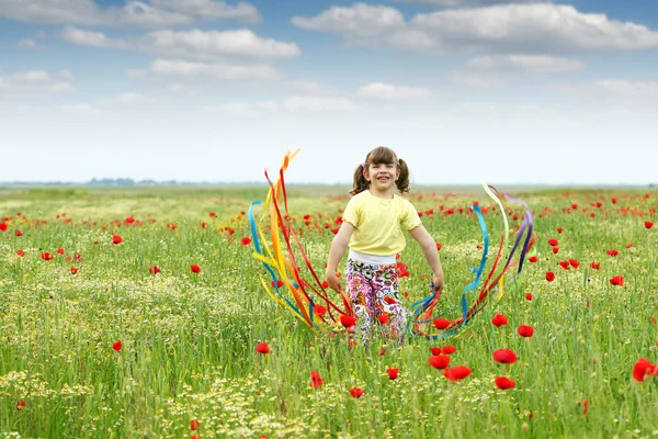 Heureuse petite fille agitant avec des rubans colorés sur prairie — Photo