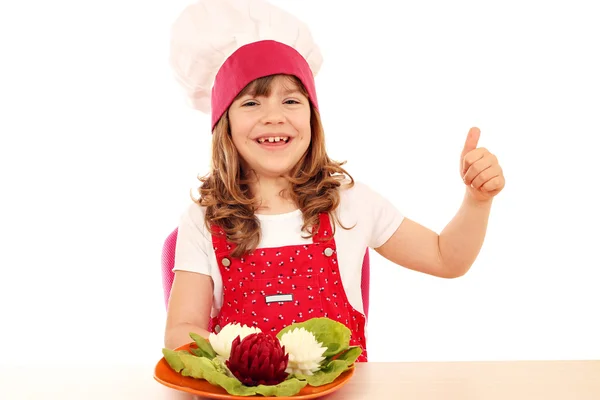 Onnellinen pieni tyttö kokki peukalolla ylös ja koristeltu salaatti — kuvapankkivalokuva