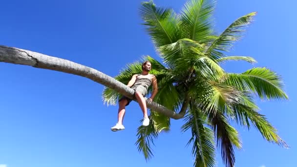 Knappe man is zitplaatsen op een palmboomyakışıklı bir palmiye ağacı üzerinde oturma — Stok video