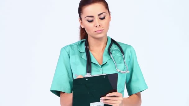 Niedliche junge Ärztin auf weißem Hintergrund macht Notizen — Stockvideo