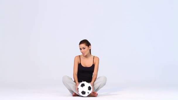 Sportos nő, futball labda, ő ül a fehér háttér — Stock videók