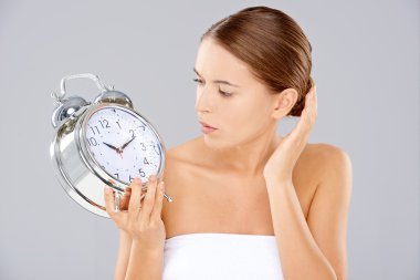 Woman looking at an alarm clock in consternation clipart