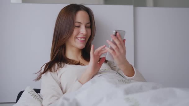 Glad woman browsing mobile phone on bed — Vídeo de Stock