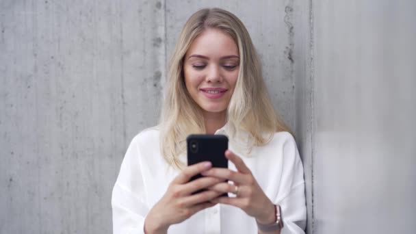 Mulher sorridente usando smartphone perto da parede — Vídeo de Stock