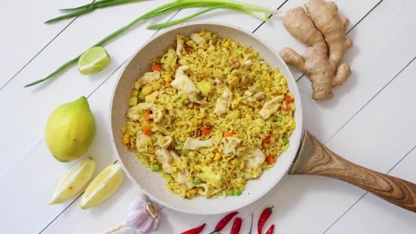 Вкусный жареный рис с курицей и овощами подается на сковороде. Размещен на белом деревянном столе — стоковое видео
