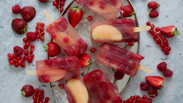 Popsicles maison à la framboise, à la fraise, aux pommes et aux groseilles sur plaque métallique avec des baies glacées assorties — Video