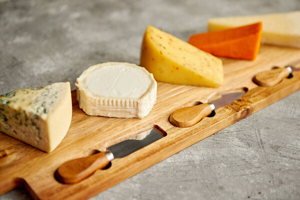 Assortment of various kinds of cheeses served on wooden board with fork and knives Royalty Free Stock Photos