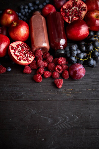 Various fresh red, purple black fruits. Mix of fruits and bottled juices on black Stock Photo