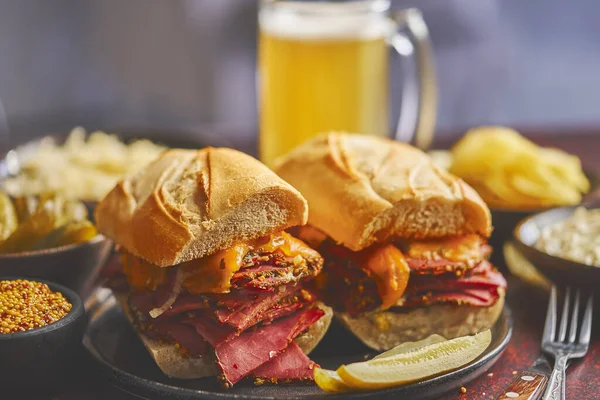 Heerlijke pastrami vlees sandwiches geserveerd met glas bier, augurken, chips en zijkanten. — Stockfoto