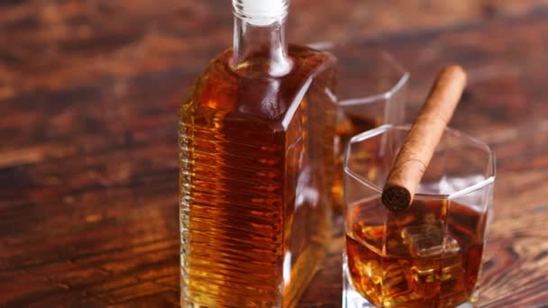 Botella de whisky con dos vasos y cigarro cubano colocado sobre mesa de madera rústica — Vídeos de Stock