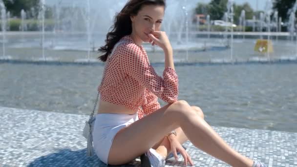身着五颜六色的夏装的漂亮女孩坐在喷泉旁 面带微笑 夏季时尚看女士 — 图库视频影像