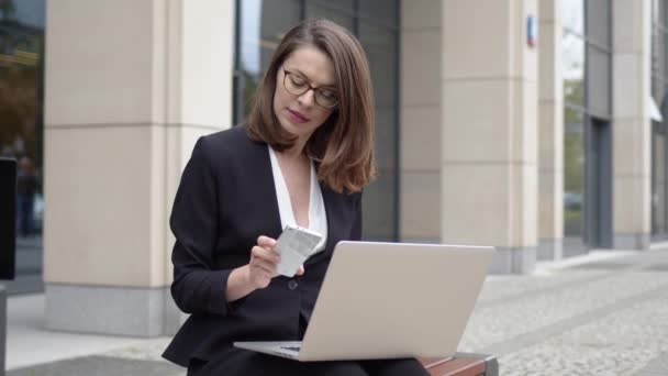有重点的年轻女性 留着短发 身穿黑色正装 坐在长椅上 写字楼在笔记本电脑上阅读紧急邮件 — 图库视频影像