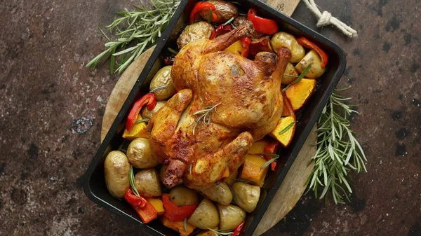 Whole roasted turkey or chicken with pepper, pumpkin, potatoes, carrots and greens in baking dish. Top view, flat lay