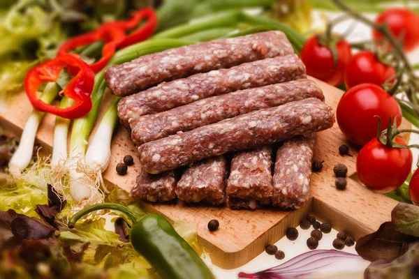 Raw kebapcheta with vegetables on wooden board — Stock Photo, Image