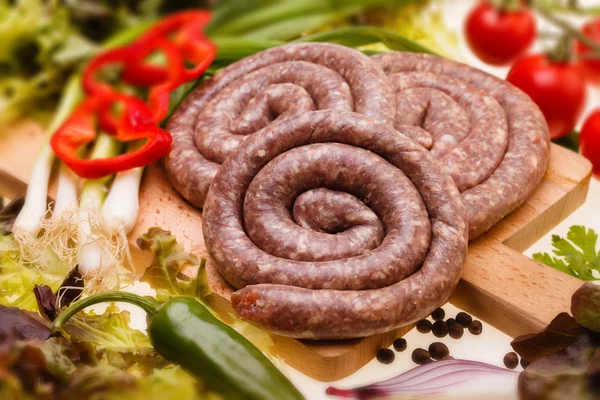 Salchichas búlgaras crudas con verduras sobre tabla de madera — Foto de Stock