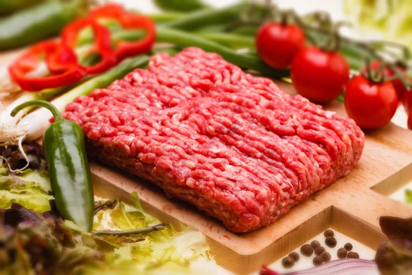 Raw minced meat with vegetables on wooden board — Stock Photo, Image