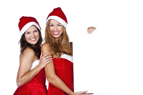 Beautiful friends wearing santa claus clothes show white blank — Stock Photo, Image