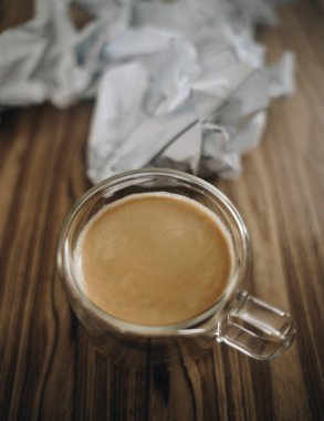 Kırışmış kağıt topların önünde küçük cam bir fincanda espresso.