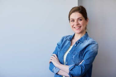 Tek başına gülümseyen ve kolları çapraz duran mavi gömlekli bir kadın..