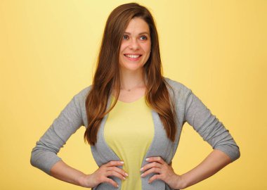 Gülümseyen kadın elleri kalçasında ve başka tarafa bakıyor. Sarı arka planda izole edilmiş kadın portresi.