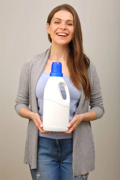 Woman in casual clothes blue shirt and jeans holding laundry detergent in white big bottle.