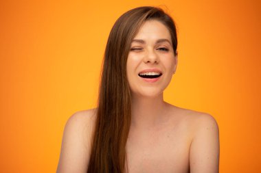 Uzun saçlı, çıplak omuzlu, göz kırpan kadın. İzole edilmiş kadın portresi turuncu arka planda..