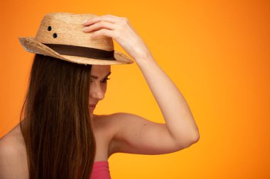 Meksika şapkasına dokunup, aşağıya bakan çıplak bakışlı genç bir kadın. Turuncu arka planda izole edilmiş yüz resmi..