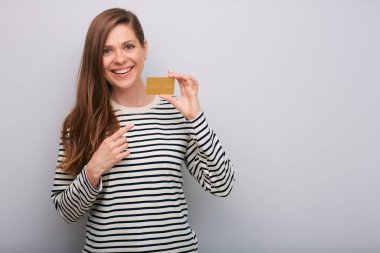 Elinde kredi kartıyla gülümseyen ve izole edilmiş bir portreyi işaret eden kadın. Uzun saçlı, çizgili sıradan gömlekli genç bir kadın..