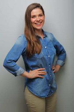 Elleri belinde gülümseyen bir kadın, gri duvar arkasında izole edilmiş bir portre. Dişleri olan geniş bir gülümseme.