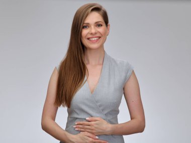 Gülümseyen iş kadınının elleri karnında. Gri iş elbisesi giyen, uzun saçlı güzel bir kızın izole edilmiş portresi..