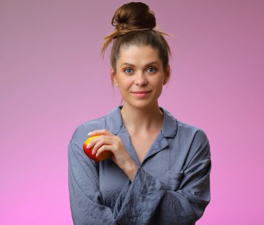 Elma tutan gülümseyen kadın pijaması, pembe kadın portresi üzerinde izole edilmiş.