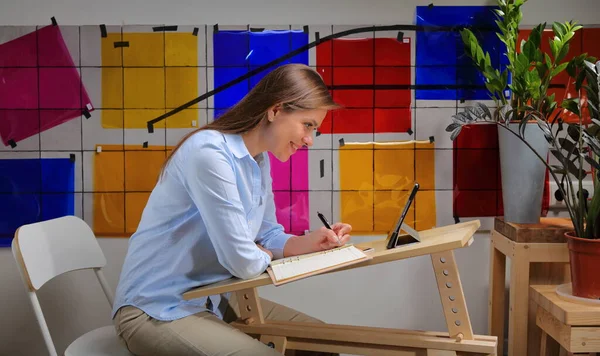 Woman designer working at table deck with Bauhaus style color palette on wall.