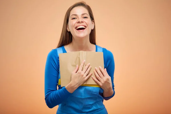Happy woman student or worker in overalls holding open book on chest. isolated on beige.