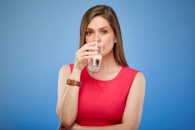 Kırmızılı gülümseyen genç bayan camdan içme suyu, mavi arka planda izole edilmiş bir portre..