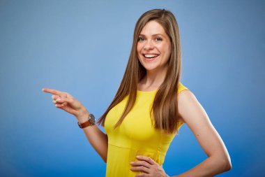 Kadın gülümsüyor ve parmağıyla işaret ediyor. Mavi arka planda izole edilmiş kadın portresi.