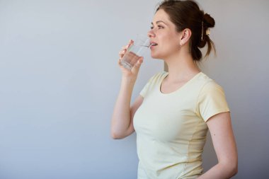 Gülümseyen ve su içen kadın gözlerini kaçırıyor. Sıradan giysili kız izole edilmiş portre..