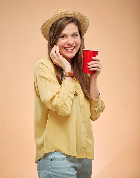 微笑的女人用黄色背景隔离了肖像 戴着草帽的年轻女士拿着红咖啡杯 — 图库照片