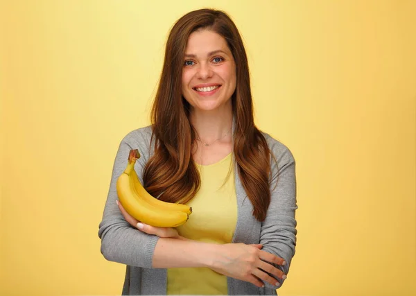 Smiling woman holding bananas fruits isolated on yellow studio back.